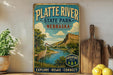 A vintage-style sign for Platete River State Park in Nebraska, featuring a scenic illustration of a river, mountains, and a bird.