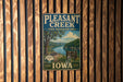 A vintage metal sign for Pleasant Creek State Recreation Area in Iowa, featuring a scenic landscape with a river, trees, and a cabin.