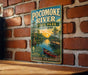 A vintage-style metal sign for Pocomoke River State Park, Maryland, featuring a scenic illustration of the river, a dock, and a boat.