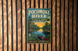 A vintage-style metal sign for Pocomoke River State Park in Maryland, featuring a scenic illustration of the river, palm trees, and a boat.