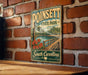 A vintage metal sign for Poinsett State Park in South Carolina, featuring a scenic image of a wooden bridge and a river with flowers.