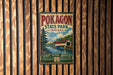 A vintage metal sign for Pokagon State Park, Indiana, featuring a scenic illustration of a covered bridge and a river.