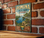 A vintage-style metal sign for Pomona State Park in Kansas, featuring a scenic landscape with a river and mountains.