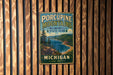 A vintage metal sign for Porcupine Mountains Wilderness State Park in Michigan, featuring a scenic landscape with a lake and mountains.