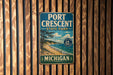 A vintage metal sign for Port Crescent State Park in Michigan, featuring a scenic landscape with a beach, mountains, and a lake.