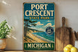 A vintage-style sign for Port Crescent State Park in Michigan, featuring a scenic beach landscape with pine trees and a lake.