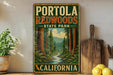 A vintage-style sign for Portola Redwoods State Park in California, featuring a scenic illustration of the park's forest and a winding river.