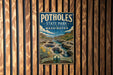 A vintage-style metal sign for Potholes State Park in Washington, featuring a scenic landscape with a river, mountains, and a waterfall.