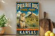 A vintage-style metal sign for Prairie Dog State Park in Kansas, featuring an illustration of a prairie dog in a field with a mountain in the background.