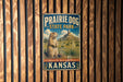 A vintage metal sign for Prairie Dog State Park in Kansas, featuring an illustration of a prairie dog in a grassy field with mountains in the background.