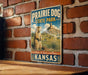 A vintage metal sign for Prairie Dog State Park in Kansas, featuring an illustration of a prairie dog in a grassy field with mountains in the background.