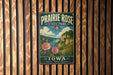 A vintage-style metal sign for Prairie Rose State Park in Iowa, featuring a scenic landscape with a river, cliffs, and flowers.