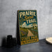 A vintage-style sign for the Prairie Spirit Trail in Kansas, featuring a scenic illustration of a path leading through a rural landscape with a river and fields.