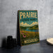 A vintage-style sign for Prairie State Park in Missouri, featuring a scenic landscape with a river, grass, and flowers.