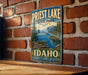 A vintage metal sign for Priest Lake State Park in Idaho, featuring a scenic landscape with mountains, trees, and a lake.