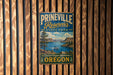 A vintage metal sign for Prineville Reservoir State Park, featuring a scenic landscape with a lake, mountains, and a boat.
