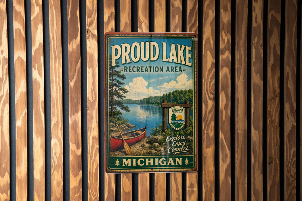 A vintage metal sign for "Proud Lake Recreation Area" in Michigan, featuring a scenic image of a lake, canoe, and surrounding forest.