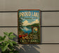 A metal sign on a wall that says "Proud Lake Recreation Area" and features a scenic image of a lake with a canoe.