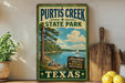 A vintage-style sign for Purtis Creek State Park in Texas, featuring a scenic illustration of a lake, pine trees, and a sailboat.