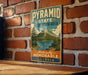 A vintage-style metal sign with the text "PYRAMID STATE RECREATION AREA" and "Naturally Memorable ILLINOIS" is displayed on a brick wall.