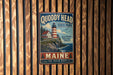 A vintage metal sign for Quoddy Head State Park in Maine, featuring a lighthouse and coastal scenery.