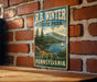 A vintage-style metal sign for R.B. Winter State Park in Pennsylvania, featuring a scenic landscape with a lake, mountains, and a sailboat.