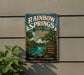 A vintage-style metal sign for Rainbow Springs State Park in Florida, featuring a tropical landscape with a rainbow, palm trees, and a body of water.