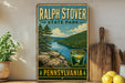 A vintage-style metal sign for Ralph Stover State Park in Pennsylvania, featuring a scenic landscape with a river, mountains, and pine trees.