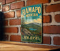 A vintage metal sign for Ramapo Mountain State Forest in New Jersey, featuring a scenic landscape with mountains, trees, and a lake.