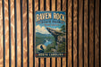 A vintage-style metal sign for Raven Rock State Park in North Carolina, featuring a scenic mountain landscape with a waterfall.
