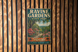 A vintage metal sign for Ravine Gardens State Park in Florida, featuring a tropical landscape with palm trees, flowers, and a winding path.