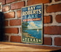 A vintage-style sign for Ray Roberts Lake, a state park in Texas, featuring a scenic illustration of a lake with a sailboat and a tree-lined shore.