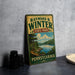 A vintage-style metal sign for Raymond Winter State Park in Pennsylvania, featuring a scenic landscape with a lake and mountains.