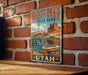 A vintage-style metal sign for Red Fleet State Park in Utah, featuring a scenic image of a boat on a lake surrounded by mountains.