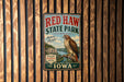 A vintage metal sign for Red Haw State Park in Iowa, featuring a hawk perched on a tree branch and the text "Red Haw State Park" prominently displayed.