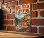 A vintage-style metal sign for Red Rock Canyon State Park in Oklahoma, featuring a scenic illustration of the canyon landscape.