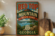 A vintage-style sign for Red Top Mountain State Park in Georgia, featuring a scenic landscape with a lake, mountains, and a sailboat.