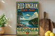 A vintage-style sign for Reed Bingham State Park in Georgia, featuring a scenic landscape with a lake and forest.