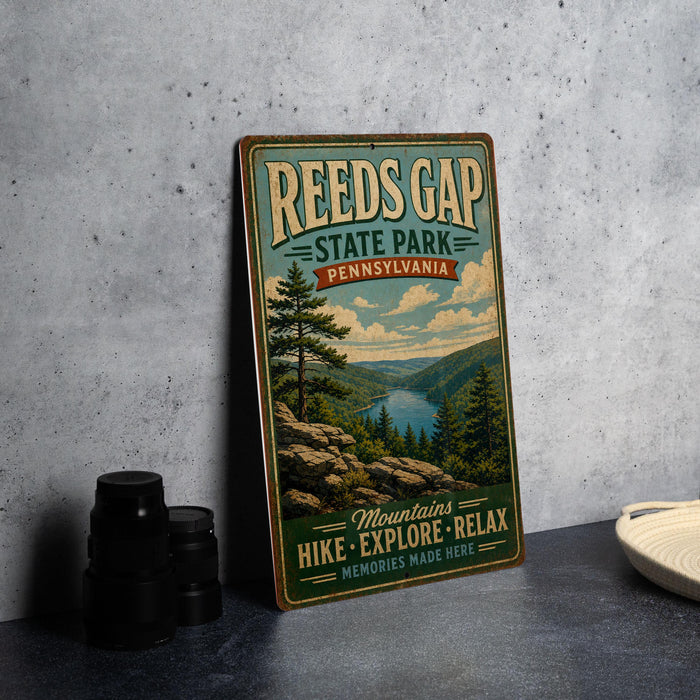 A vintage-style metal sign for Reeds Gap State Park in Pennsylvania, featuring a scenic mountain landscape with a river and pine trees.