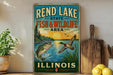 A vintage-style metal sign for the Rend Lake State Fish & Wildlife Area in Illinois, featuring illustrations of fish and wildlife against a sunset backdrop.