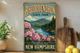 A vintage-style sign for Rhododendron State Park in New Hampshire, featuring a scenic landscape with mountains, a river, and pink flowers.