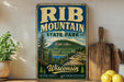 A vintage-style sign for Rib Mountain State Park in Wisconsin, featuring a scenic mountain landscape with pine trees and a lake.
