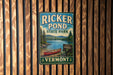 A vintage-style metal sign for Ricker Pond State Park in Vermont, featuring a red canoe and a scenic landscape.