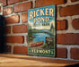 A vintage-style metal sign for Ricker Pond State Park in Vermont, featuring a scenic image of a lake with a red canoe and a sign indicating the location.