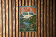 A vintage metal sign for Ringwood State Park in New Jersey, featuring a scenic landscape with a lake and mountains.