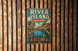 A vintage-style metal sign for River Island State Park in Arizona, featuring a scenic landscape with palm trees, mountains, and a bird.