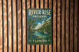 A vintage-style metal sign for River Rise Preserve State Park in Florida, featuring a tropical landscape with palm trees and a bird.