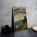 A vintage-style metal sign for Robert Louis Stevenson's State Park in California, featuring a scenic landscape with mountains, a beach, and a lighthouse.
