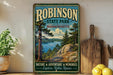 A vintage-style sign for Robinson State Park in Massachusetts, featuring a scenic landscape with pine trees, a lake, and mountains.
