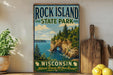 A vintage-style sign for Rock Island State Park in Wisconsin, featuring a scenic landscape with cliffs, water, and pine trees.